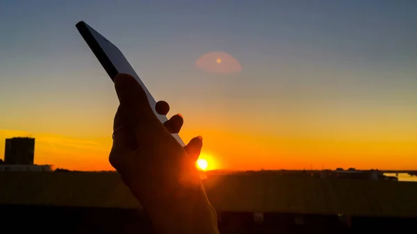 Woman silhouette using smartphone in city at sunset