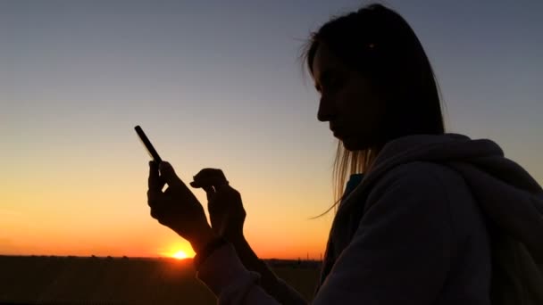 Жінка силует за допомогою смартфона в місті на заході сонця — стокове відео