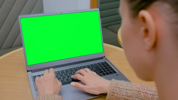 Mujer escribiendo en el teclado del ordenador portátil con pantalla verde en blanco en la cafetería — Vídeos de Stock