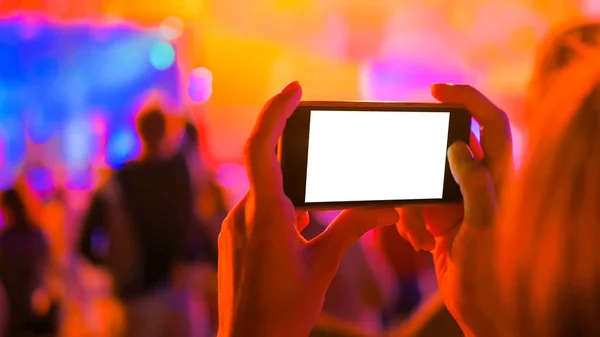 Mulher mão silhueta segurando smartphone com display branco vazio no concerto — Fotografia de Stock