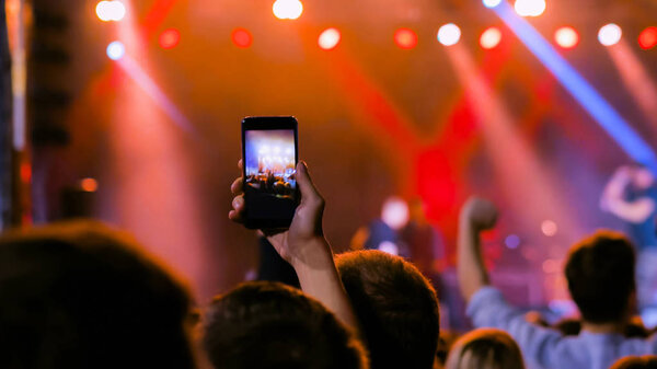People hands silhouette recording video of live music concert with smartphone