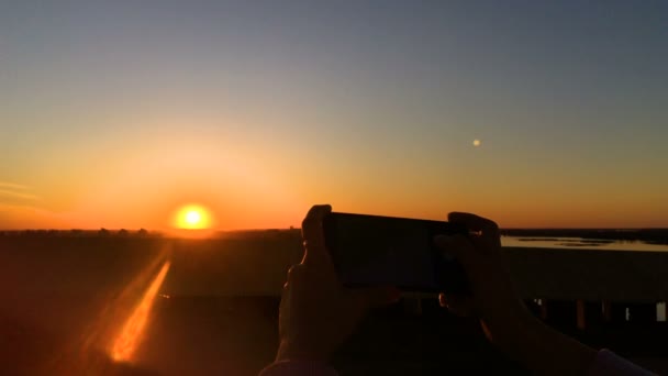 Mujer tomando fotos del atardecer con smartphone en la ciudad — Vídeos de Stock