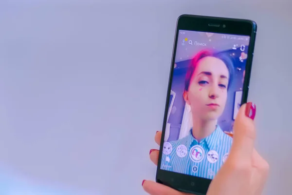 スマートフォンでフェイスマスクを持つSnapchatマルチメディアメッセージングアプリを使用している女性 ロイヤリティフリーのストック画像