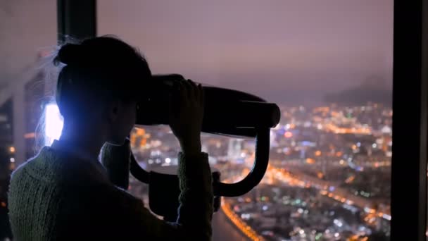 Jovem olhando através do telescópio turístico e explorando paisagem urbana noturna — Vídeo de Stock
