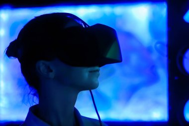 Karanlık etkileşimli sergide sanal gerçeklik kulaklığı kullanan genç bir kadın.