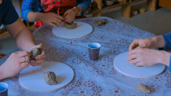 Three people making clay mugs in pottery studio