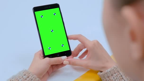Женщина смотрит на черное устройство смартфона с пустым зеленым экраном — стоковое видео