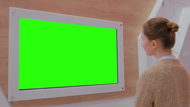 Mujer mirando la pared de visualización verde en blanco en la exposición - concepto de pantalla verde — Vídeos de Stock