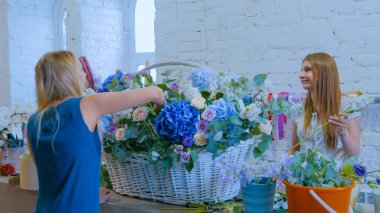 Çiçekçide çiçeklerle büyük bir sepet yapan iki kadın.