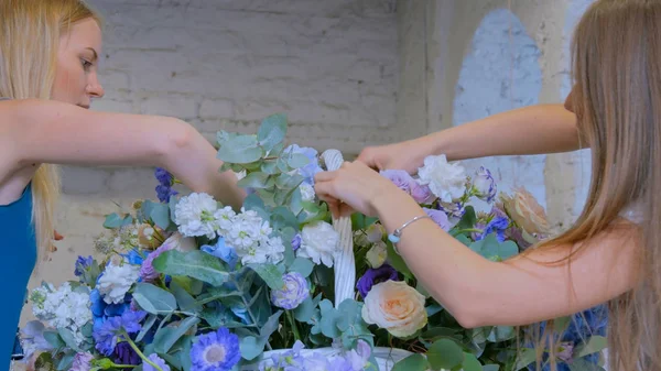 Two women florists making large floral basket with flowers at flower shop