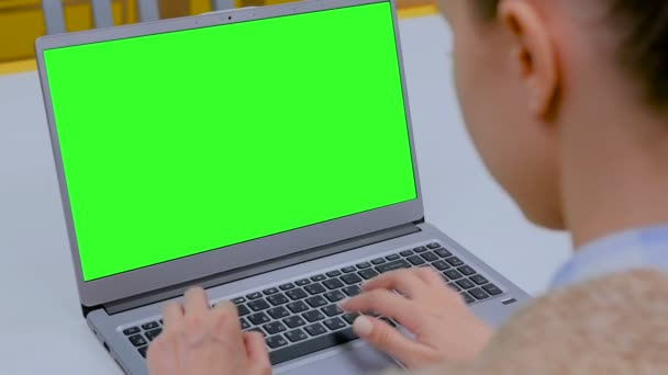 Mujer escribiendo en el teclado del ordenador portátil con pantalla verde en blanco en la cafetería — Vídeos de Stock