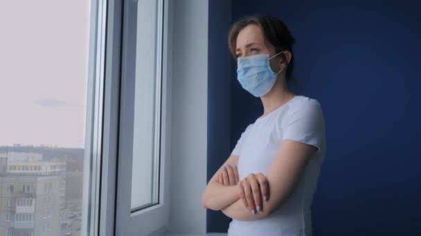 スローモーション:医療面マスクを着用し、窓の外を見る女性 — ストック動画