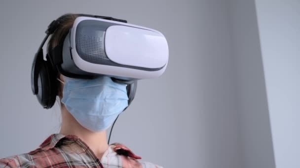 Młoda kobieta ubrana w medyczną maskę twarzy i zestaw słuchawkowy wirtualnej rzeczywistości - koncepcja VR — Wideo stockowe