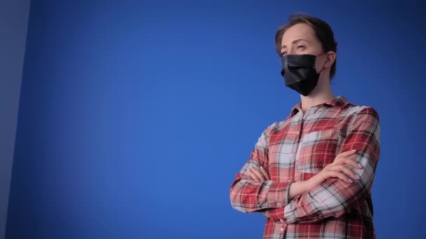 Slow motion: vrouw met zwart medisch gezichtsmasker, wegkijkend in blauwe kamer — Stockvideo