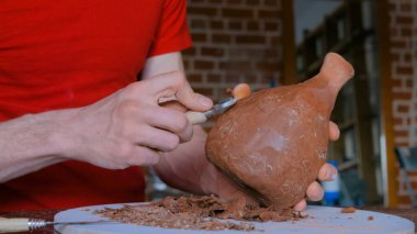 Profesyonel çömlekçi, çömlek atölyesinde özel bir aletle kuru kil kavanozunu şekillendiriyor.