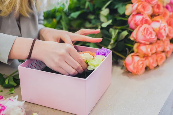 Woman floral artist, florist making gift box with flowers on table - close up