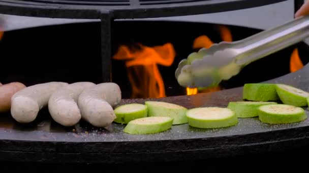 Zeitlupe: Koch grillt Würstchen und Zucchini auf Kohlenbecken mit heißer Flamme — Stockvideo