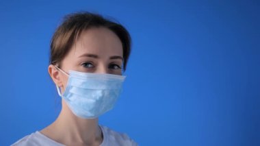 Tıbbi yüz maskesi takan bir kadın, kameraya bakıyor, karantina konseptini kapatıyor.