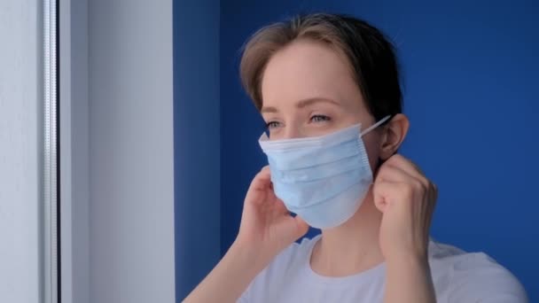 Movimento lento: mulher sorridente colocando máscara facial médica e olhando para longe — Vídeo de Stock