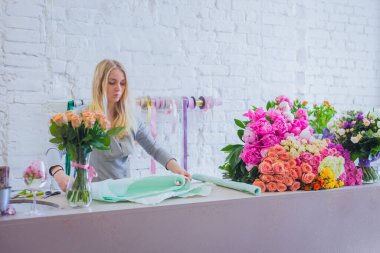 Çiçekçide buket için kağıt kesen bir çiçekçi.