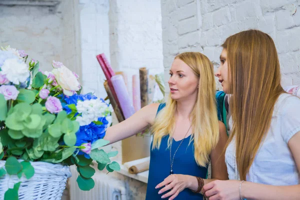 Two women florists making large floral basket with flowers in bright room