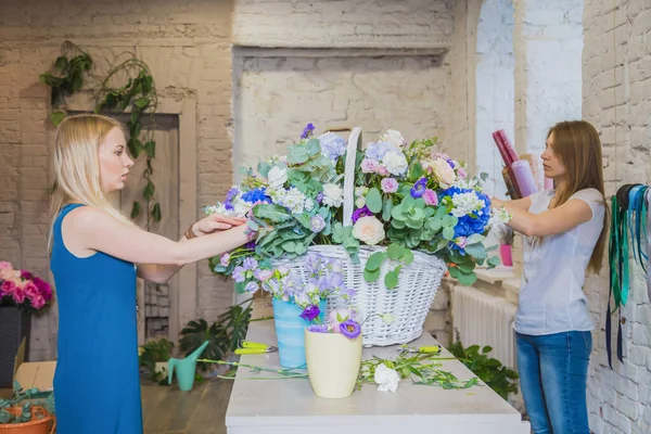 Two women florists making large floral basket with flowers in bright room