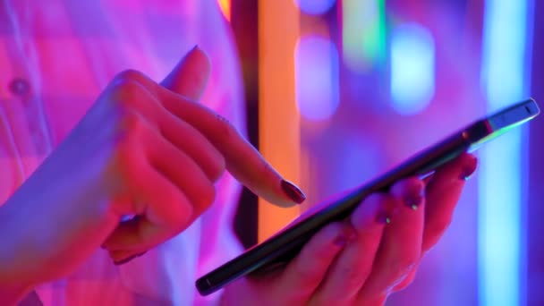 Vista de cerca: manos de mujer usando teléfono inteligente contra fondo colorido luz — Vídeo de stock