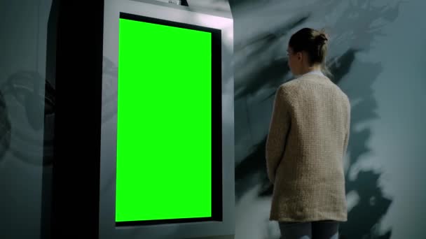 Woman looking at blank green display kiosk at exhibition - green screen concept — Stock Video