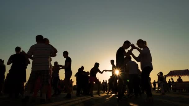 Люди силуети вчаться танцювати на міській набережній під час заходу сонця - повільно. — стокове відео
