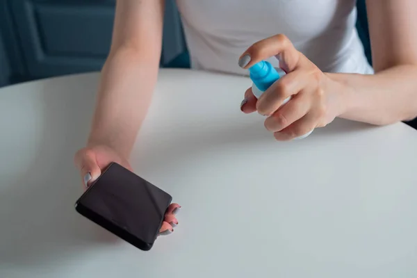 Женщина чистит смартфон с антисептиком на белом столе - концепция дезинфекции — стоковое фото