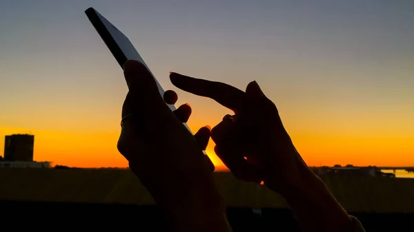 Woman silhouette using smartphone in city at sunset