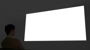 Kadın büyük beyaz duvar ekranına bakıyor. Sinema taklit ediyor.