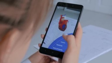 Artırılmış gerçeklik uygulaması olan akıllı telefon kullanan bir kadın. İnsan kalbinin 3D modeli.