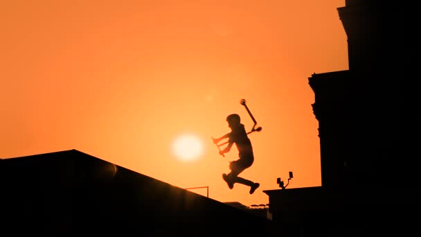 Silhueta adolescente mostrando truques de salto alto em scooter ao pôr do sol - câmera lenta — Vídeo de Stock