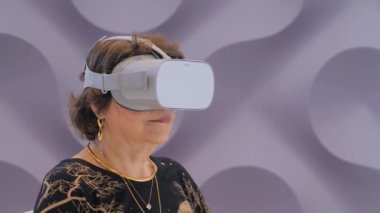 VR teknoloji sergisinde sanal gerçeklik kulaklığı kullanan yaşlı bir kadın.