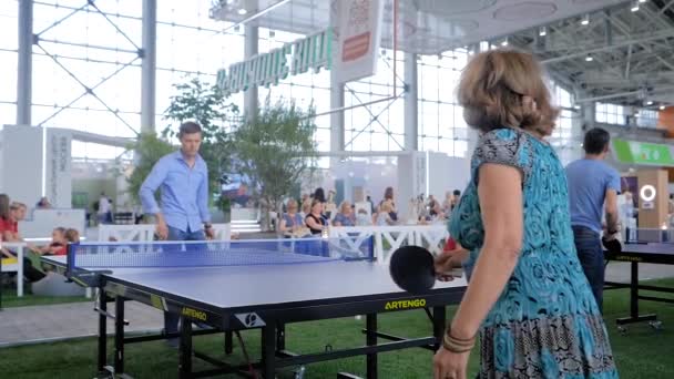 Ung man och äldre kvinna spelar pingis bordtennis på sportutställning — Stockvideo