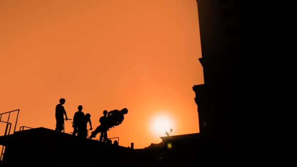 Movimento lento: silhueta adolescente mostrando truques de salto alto em scooter ao pôr do sol — Vídeo de Stock