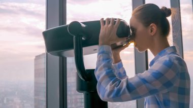 Turist teleskopundan bakan ve şehir manzarasını keşfeden bir kadın.