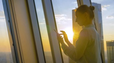 Günbatımı şehir manzarasına karşı akıllı telefon kullanan kadın