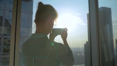 Gökdelen penceresinden şehrin akıllı telefonuyla fotoğraf çeken bir kadın