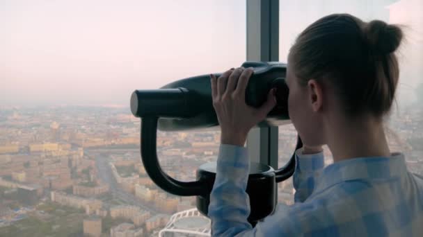 Young woman looking through tourist telescope, exploring spectacular cityscape — Stock Video