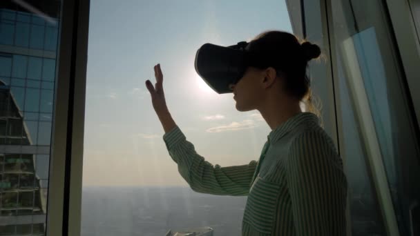 Молода жінка використовує гарнітуру віртуальної реальності проти вікна хмарочоса концепція VR — стокове відео
