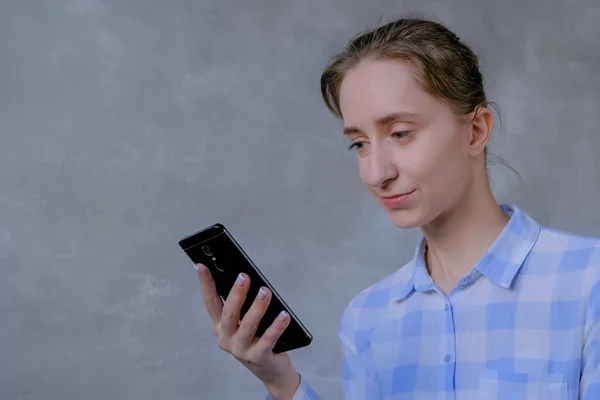 Retrato de mulher em camisa xadrez usando smartphone em quarto cinza — Fotografia de Stock