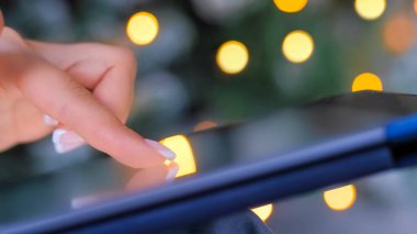 Dokunmatik ekran tableti kullanan bir kadın, Noel ışığı arka planı - kapat