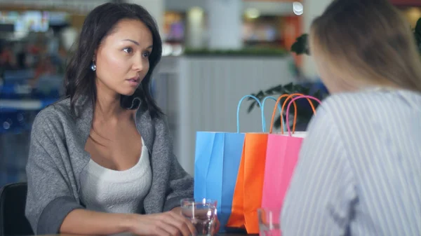 Dos mujeres jóvenes discutiendo algo sentadas en un café en el centro comercial — Foto de Stock