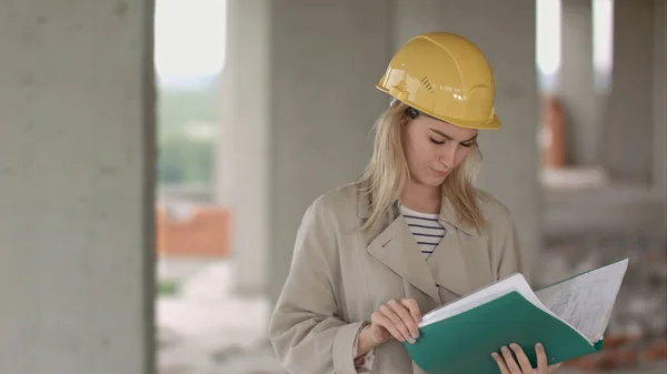 Jovem arquiteta engenheira de construção em um canteiro de obras eximaining documentos — Fotografia de Stock