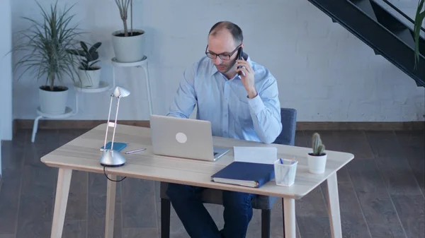 Бизнесмен работает за компьютером, разговаривая на смартфоне — стоковое фото