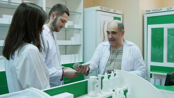 Farmacéutico Senior Dando Sueldo Dólares Sus Jóvenes Colegas Farmacia Cerca —  Fotos de Stock