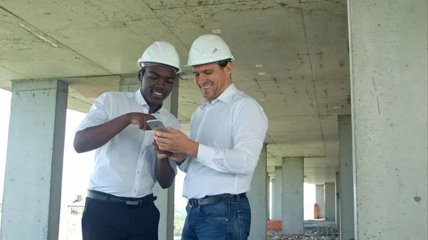 Construtores de construção sorrindo enquanto usa smartphone no local — Fotografia de Stock