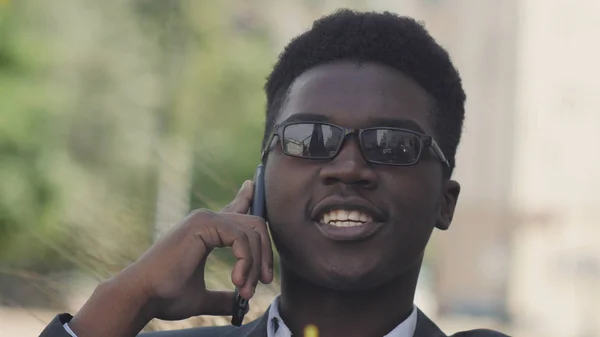 Porträtt av glada afrikanska man sitter utanför talar på smart phone — Stockfoto